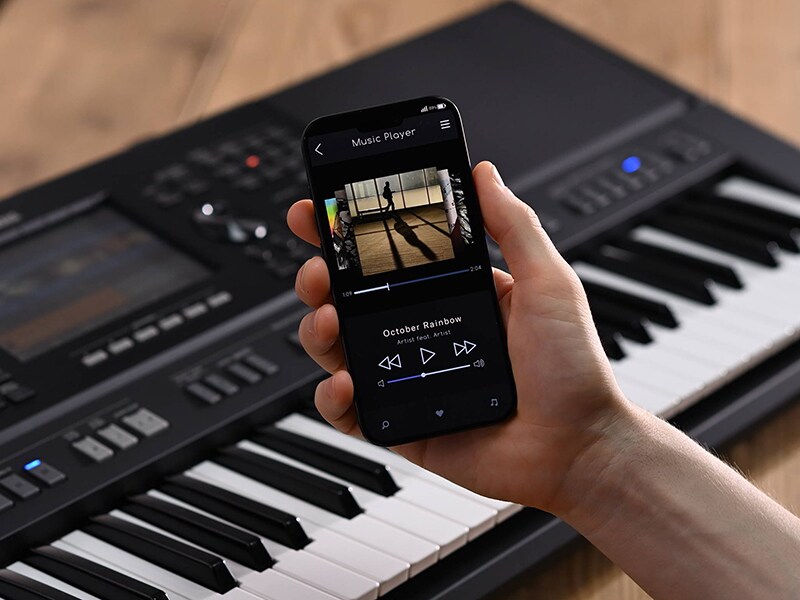 Aranżer Yamaha Arranger Workstation PSR-SX920 oraz dłoń trzymająca smartfon z ekranem odtwarzacza muzyki