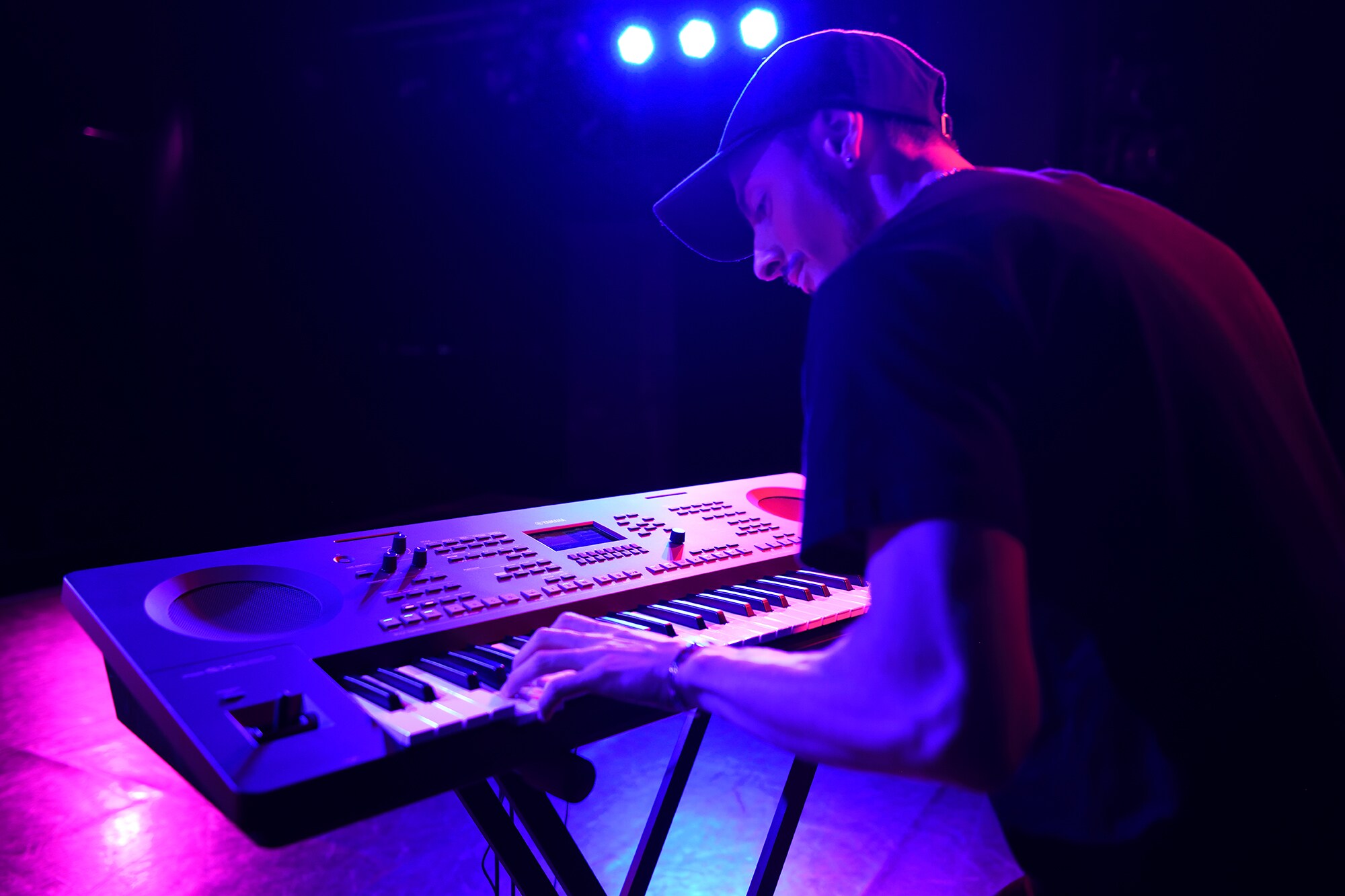 Osoba grająca na stacji roboczej Arranger Workstation marki Yamaha na statywie w oświetleniu scenicznym