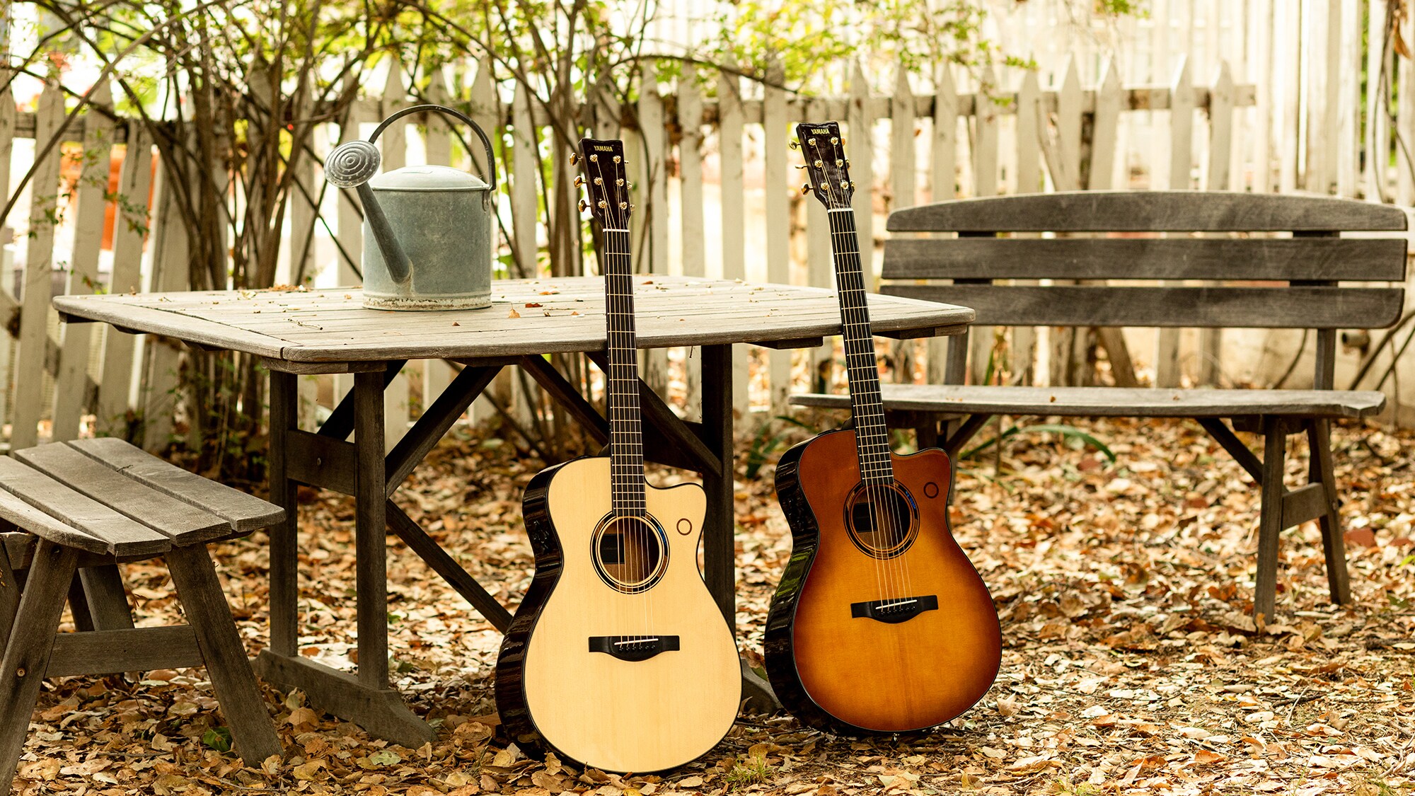 Two acoustic guitars resting by a wooden bench outdoors.