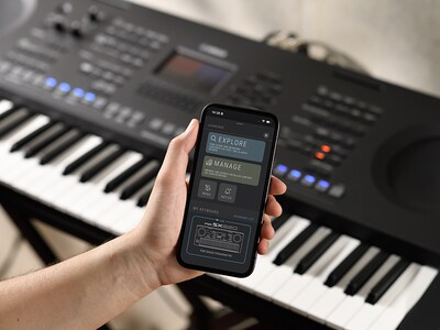 PSR-SX620 oraz dłoń trzymająca smartfon z ekranem oficjalnej aplikacji Yamaha „Expansion Explorer”.